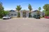 Charming apartment entrance with manicured landscaping and spacious parking area under a clear blue sky.