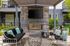 Elegant outdoor lounge with modern fireplace, sleek TV, stylish seating, and vibrant pillows under a chic pergola.