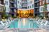 Luxurious apartment complex featuring a stunning illuminated pool area with sleek lounge chairs, surrounded by modern architecture.