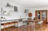 Chic communal kitchen with modern decor, featuring elegant white cabinetry, stylish bar stools, and contemporary art pieces on pristine shelves.