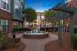 Charming apartment courtyard with a brick fountain, lush greenery, and modern pergola at sunset.