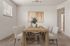 Elegant dining room with a rustic wooden table, comfortable upholstered chairs, and contemporary artwork. Natural light fills the space, enhancing the welcoming ambiance.
