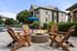 Chic outdoor lounge area with a cozy fire pit, surrounded by stylish wooden chairs and lush greenery, perfect for relaxation.