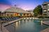 Luxurious apartment complex featuring an inviting swimming pool with elegant loungers, surrounded by lush greenery and a modern clubhouse, set against a stunning sunset backdrop.