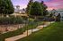 Serene apartment complex with lush greenery, elegant fencing, and a cozy pavilion under a stunning sunset sky.