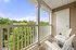 Charming apartment balcony with cozy seating, offering a serene view of lush green trees and a clear blue sky.