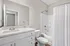 Modern bathroom with sleek vanity, large mirror, and a pristine bathtub surrounded by elegant white tiles.