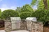 Charming outdoor cooking space featuring sleek stainless steel grills set in an elegant stone countertop, surrounded by lush greenery and a clear blue sky.