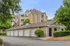 Charming apartment complex with modern architecture and individual garages, surrounded by lush greenery and a well-maintained driveway.