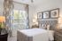 Bright and inviting bedroom featuring a plush gray upholstered bed, modern wooden nightstands, and stylish abstract wall art, with large windows for abundant natural light.
