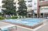 Modern apartment complex with a luxurious pool area, featuring sleek lounge chairs and vibrant greenery.