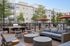 Chic outdoor patio area with modern seating and BBQ, surrounded by lush greenery and stylish apartment buildings.