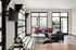 Bright living room with modern L-shaped sofa, large windows, and stylish decor featuring orange accent pillows and sleek television setup.