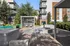 Inviting outdoor communal area featuring modern seating, shaded pergola, and a cozy fire pit, set against contemporary apartment buildings.