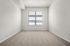 Bright and inviting bedroom space with soft carpet flooring and natural light pouring in through large window blinds.