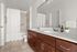 Elegant modern bathroom featuring dual sinks with wooden cabinetry, a spacious mirrored vanity, and a sleek tiled shower area with accessible grab bars.