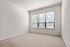 Bright and airy empty room with large window and soft carpet flooring, perfect for a cozy bedroom setup.