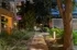 Charming night view of lush apartment walkway illuminated by modern lighting, surrounded by greenery and tranquil ambiance.