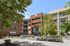 Modern apartment complex entrance featuring a stylish facade, lush greenery, and clear blue skies.