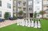 Modern apartment courtyard featuring a giant chess set on lush green grass with sleek seating and contemporary architecture.