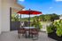 Chic outdoor terrace with vibrant red umbrella, cozy seating, and lush greenery, perfect for relaxation.