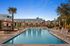 Luxurious poolside area with comfortable loungers, surrounded by lush greenery and modern apartment buildings under a vibrant evening sky.