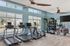 Bright and modern fitness center with treadmills, free weights, and training area, featuring large windows and stylish ceiling fans.