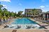 Luxurious apartment pool area with stylish lounge chairs, vibrant umbrellas, and lush palm trees, offering a resort-style oasis.