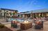 Luxurious apartment complex with a stunning poolside view, featuring stylish lounge chairs, palm trees, and a cozy fire pit under a clear blue sky.