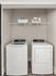 Modern laundry closet featuring a sleek washing machine and dryer set against a neutral backdrop with convenient overhead shelving.