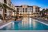 Luxurious apartment complex with modern architecture, featuring a stylish swimming pool, surrounded by palm trees and elegant lounge chairs, under a beautiful evening sky.