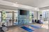 Modern apartment gym featuring mirrored walls, a vibrant accent wall, exercise equipment, and natural light streaming through large windows.