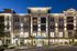 Elegant apartment building with modern lighting at dusk, featuring a welcoming leasing office entrance surrounded by lush landscaping.