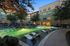 Luxury apartment complex with a stunning illuminated swimming pool surrounded by stylish lounge chairs and shaded seating areas, perfect for evening relaxation.