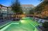 Inviting evening view of a luxury apartment complex with a sparkling outdoor pool and stylish lounge chairs, surrounded by lush greenery and modern architecture.