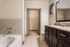 Luxurious bathroom with elegant granite countertop, chic dark wood cabinetry, and a spacious tub, leading to a walk-in closet.