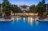 Luxurious apartment complex at dusk with a serene pool, elegant architecture, and lush greenery.