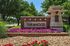 Inviting entrance of Terrawood with vibrant flowerbeds and elegant brickwork, surrounded by lush greenery.