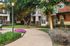 Charming apartment exterior with lush green landscaping, vibrant flowers, and inviting walking paths under soft evening lights.