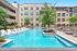 Luxury apartment complex with a sparkling swimming pool, sun loungers, and vibrant landscaping.
