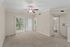 Bright and airy living room with plush carpeting, ceiling fan, and sliding glass doors opening to a scenic balcony.