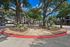 Charming apartment community entrance featuring lush landscaping, mature trees, and inviting pathways under a clear blue sky.