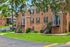 Charming brick apartment building with lush green lawns, mature trees, and inviting staircases in a tranquil neighborhood setting.