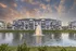 Charming modern apartment complex with serene pond and elegant fountain at sunset, offering scenic views and tranquility.