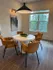 Chic dining area with modern design, featuring a round table and four plush chairs, illuminated by stylish pendant lighting, set against a backdrop of large windows and contemporary artwork.