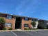 Charming brick apartment building with green landscaping and ample parking under a clear blue sky.