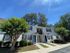 Charming white townhouse with blue doors, surrounded by lush greenery and tall trees under a clear blue sky.