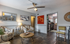 Inviting living room with artistic decor, plush patterned chairs, and a stylish ceiling fan, seamlessly leading to a modern kitchen.