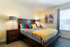 Inviting bedroom with stylish decor, colorful pillows, and soft natural light from a large window, creating a cozy and vibrant atmosphere.