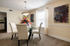 Elegant dining area with a glass table, cushioned chairs, vibrant floral centerpiece, and artistic wall decor, bathed in natural light.